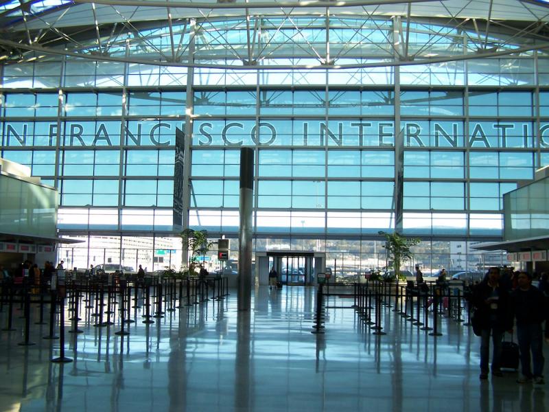 Interior of San Francisco International Airport's Harvey Milk Terminal with glass curtain wall signage and queue stanchions #1